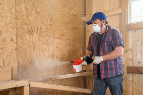 Photo of a masked man spraying the birchmeier bobby onto constructible wood. It is recommended that a mask is worn while applying this powder.